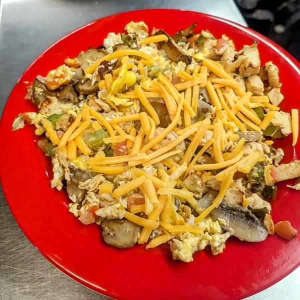A Waffle Shoppe breakfast scramble with eggs, cheese, mushrooms, and peppers on a red plate.