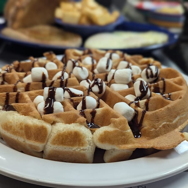 Golden Waffle Shoppe waffle topped with mini marshmallows and chocolate syrup on a white plate.