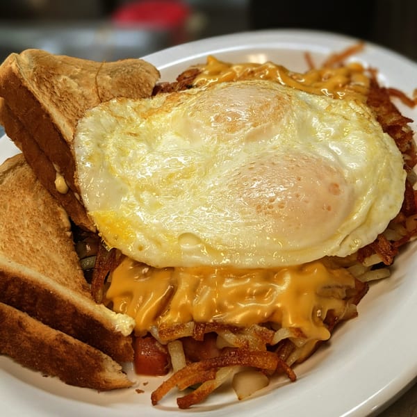 A Waffle Shoppe breakfast plate with two fried eggs, hash browns with melted cheese, and toast.
