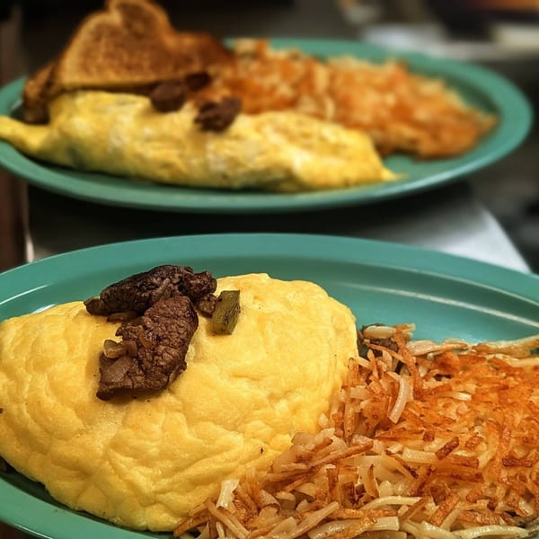 Two breakfast plates with omelets topped with steak, hash browns, and toast.