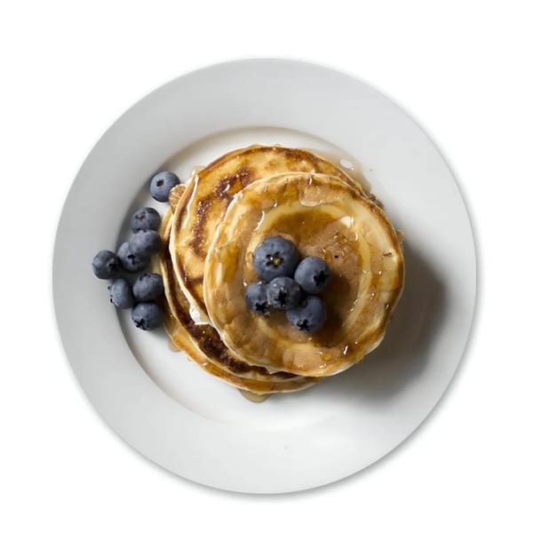 Stack of golden pancakes drizzled with syrup and topped with fresh blueberries on a white plate.