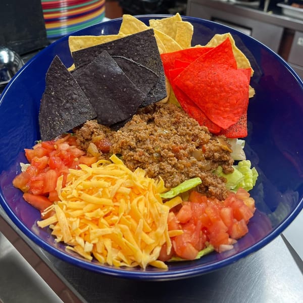 A blue bowl filled with taco salad, featuring ground meat, cheese, tomatoes, lettuce, and tortilla chips.