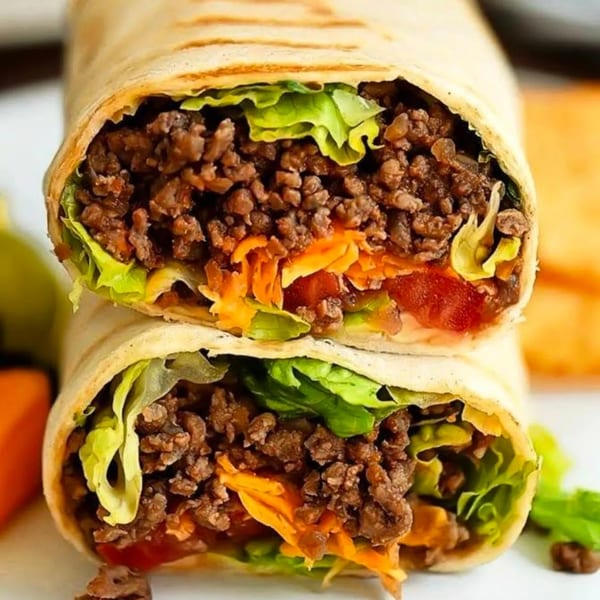 Two halves of a breakfast burrito filled with ground meat, lettuce, shredded carrots, and tomatoes.